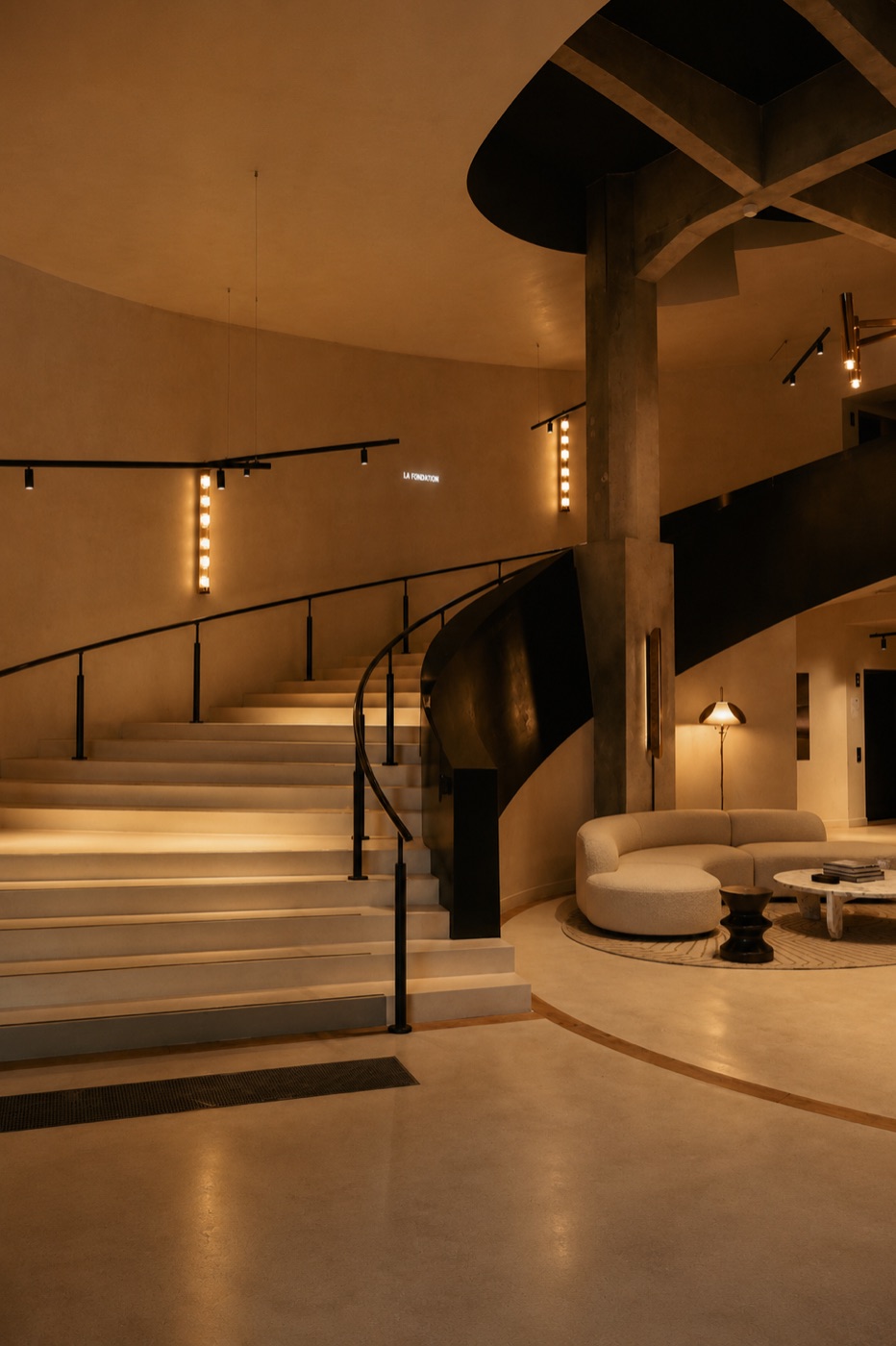 Hall et escalier courbe d’un lieu contemporain, lumière chaude rasante, La Fondation Paris